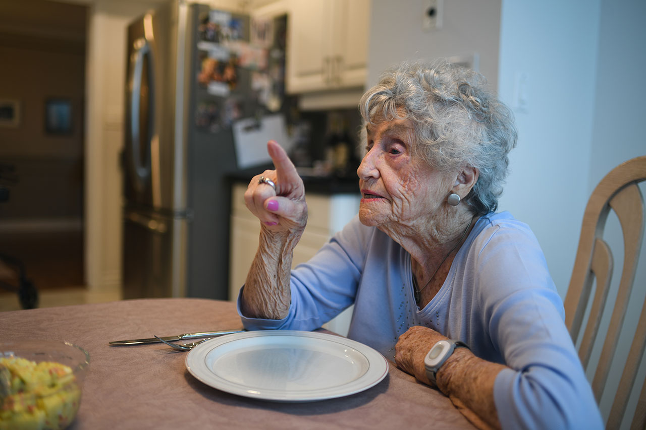 Rose Lipszyc points her right index finger while sitting on a chair at the dining table with an empty plate and cutlery.