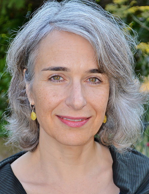 Charlotte Schallie smiling and wearing yellow stone earrings against a blurred background with some vegetation.